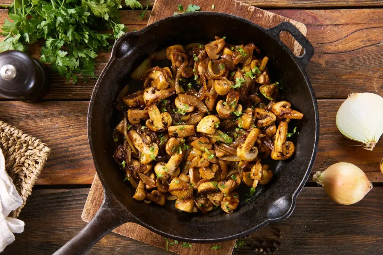 Pieczarki i cebula podsmażone na patelni, posypane natką pietruszki.