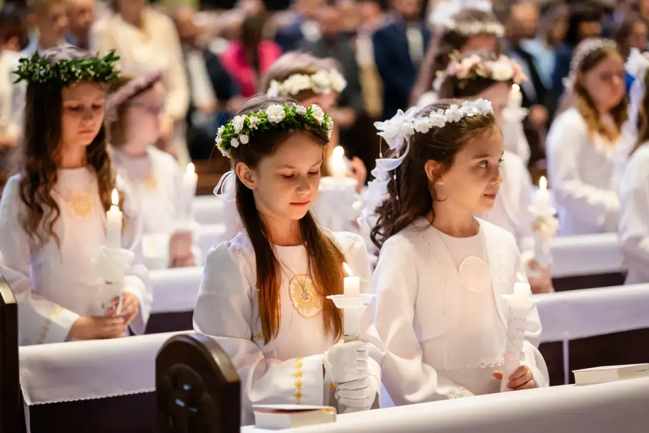 Dziewczynki w białych strojach z wiankami na głowach trzymają świece. Zastanawiasz się, ile kosztuje fotograf na komunie?