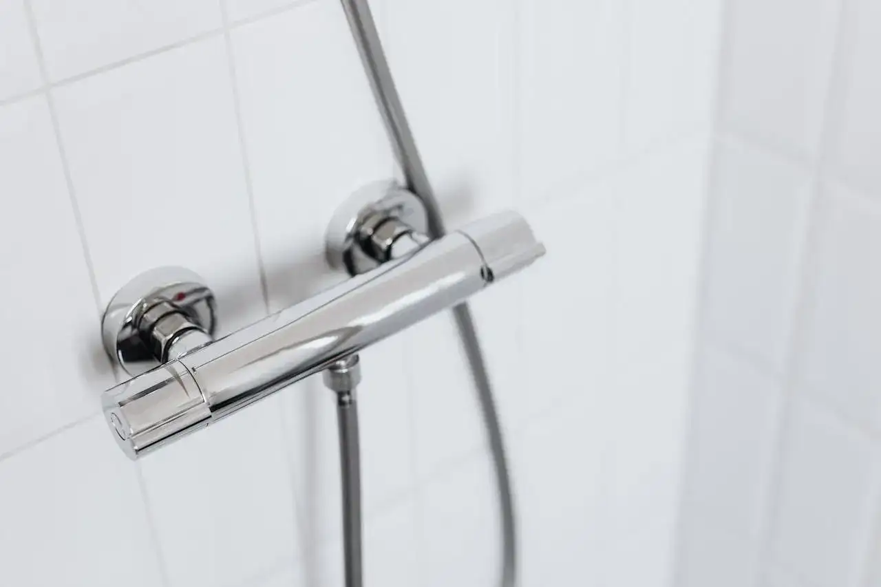 Chromowany panel prysznicowy na białej, kafelkowej ścianie. Idealny, gdy zastanawiasz się, jak zrobić prysznic na działce rekreacyjnej.