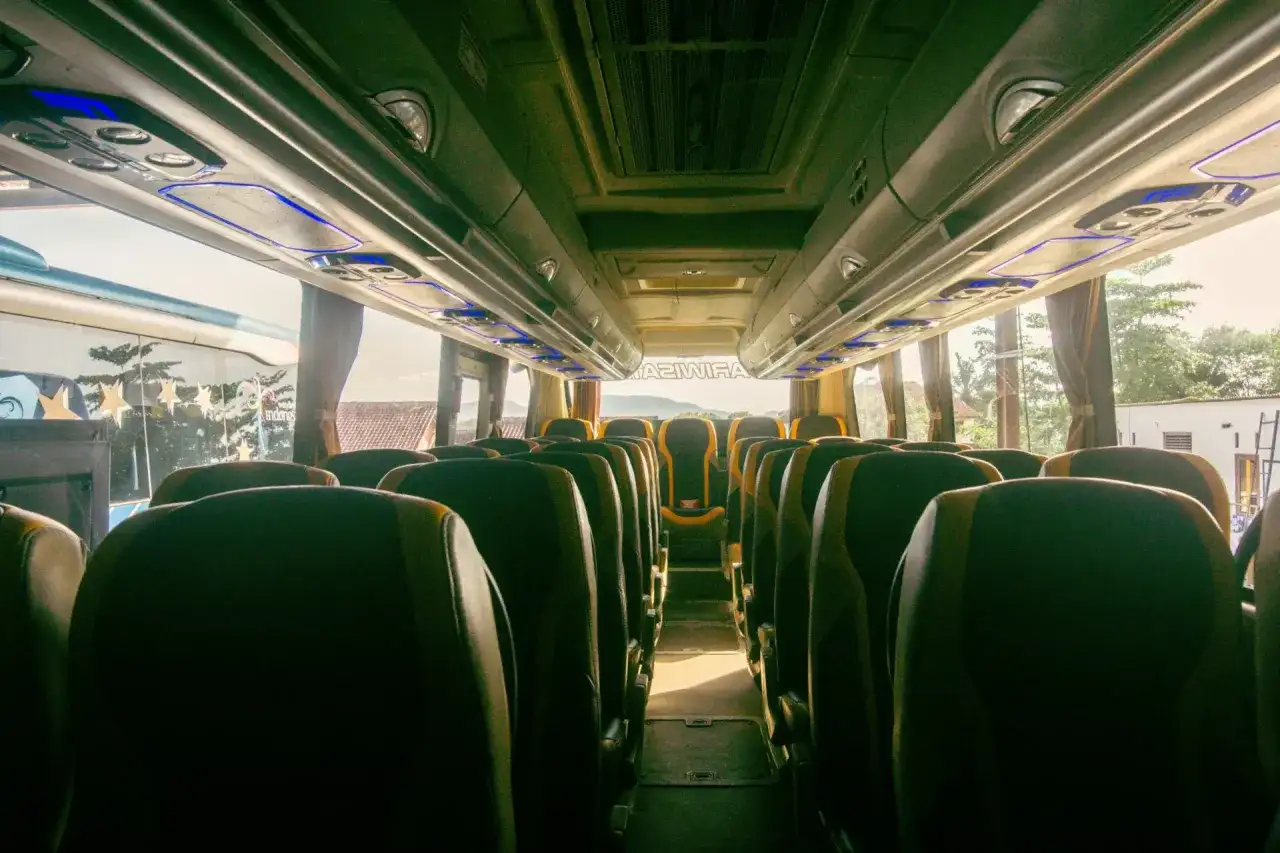 Wnętrze autobusu z rzędami ciemnych siedzeń i niebieskim oświetleniem podsufitowym.