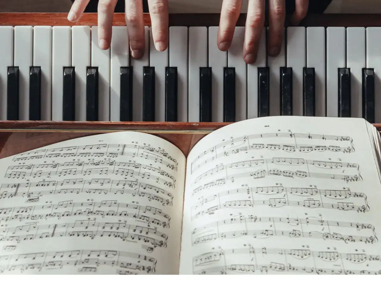 Dłonie grające na pianinie, przed nimi otwarta księga z nutami i tabelą akordów.
