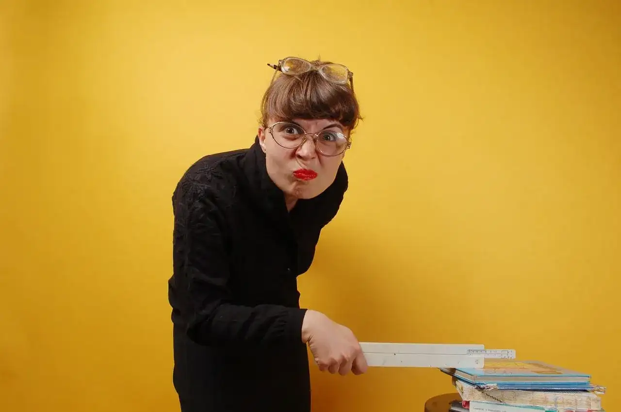 Kobieta w okularach i czarnej bluzce trzyma linijkę nad stosem książek.