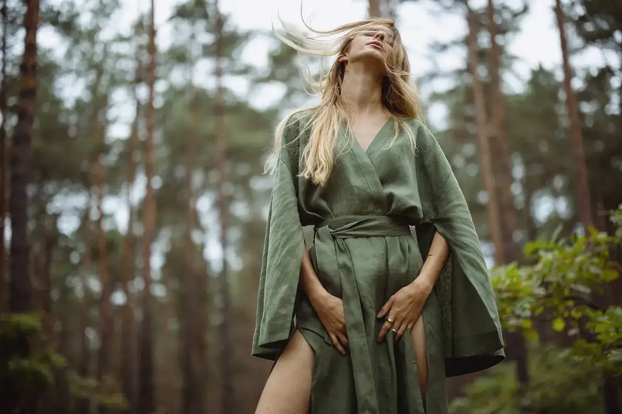 Kobieta w lnianej sukience w lesie. Włosy rozwiane przez wiatr, zmysłowa fotografia mody.