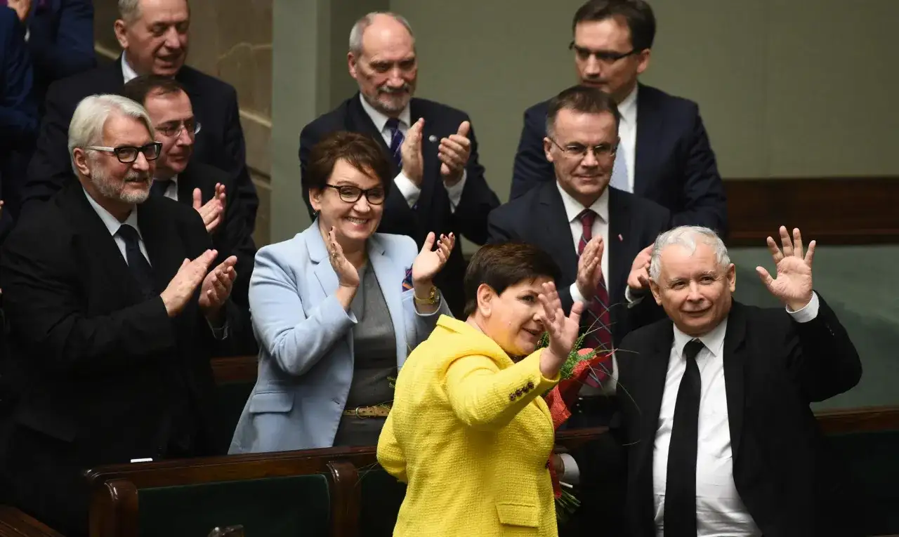 Kiedy rządził PiS, Beata Szydło w żółtej marynarce i Jarosław Kaczyński w garniturze pozdrawiają tłum.