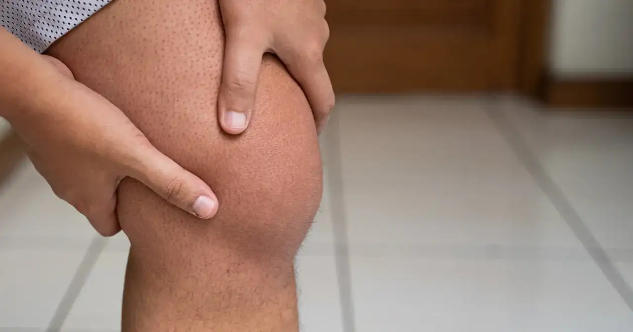 Dłoń uciska opuchnięte kolano.