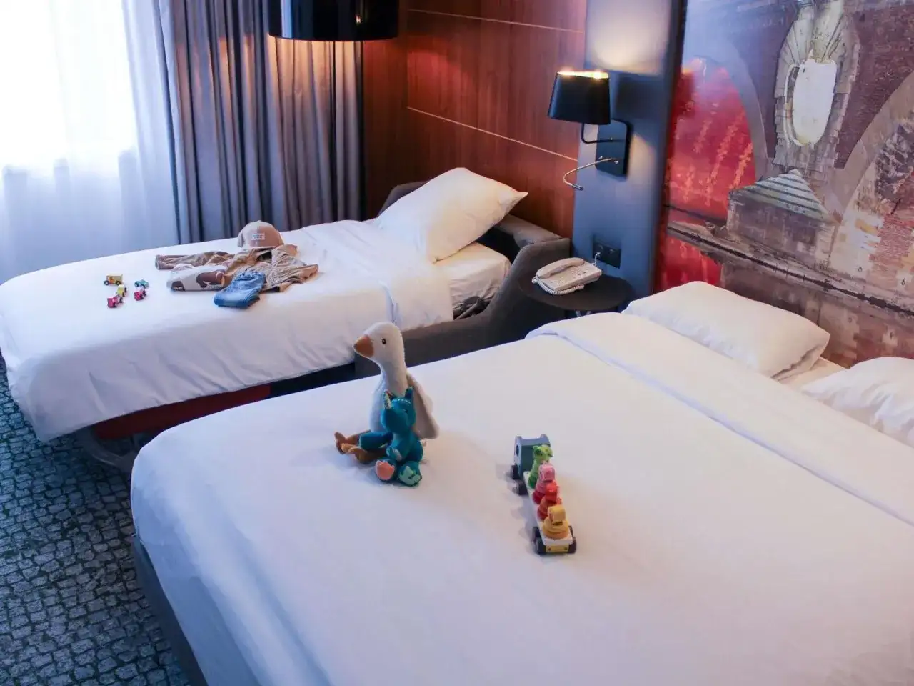 Chambre d'hôtel avec deux lits, jouets et vêtements pour enfants.