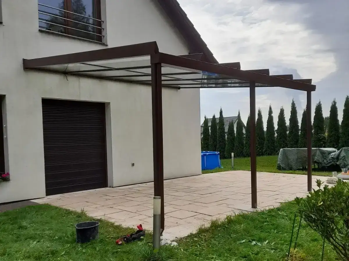 Nowoczesne zadaszenie tarasu z przezroczystym dachem, przyścienne, z brązową konstrukcją.