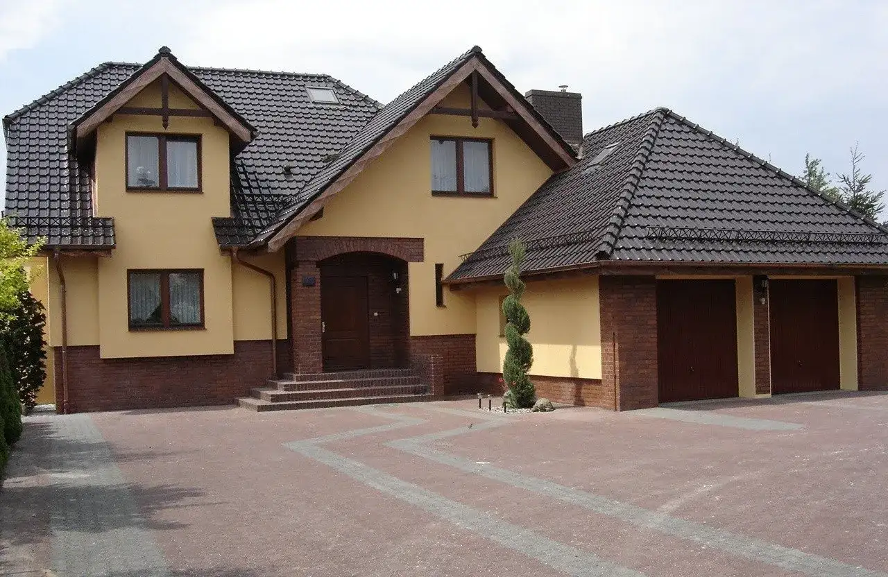 Dom z żółtą elewacją i brązowym dachem. Zastanawiasz się, ile waży dachówka? Ten dach wygląda solidnie.