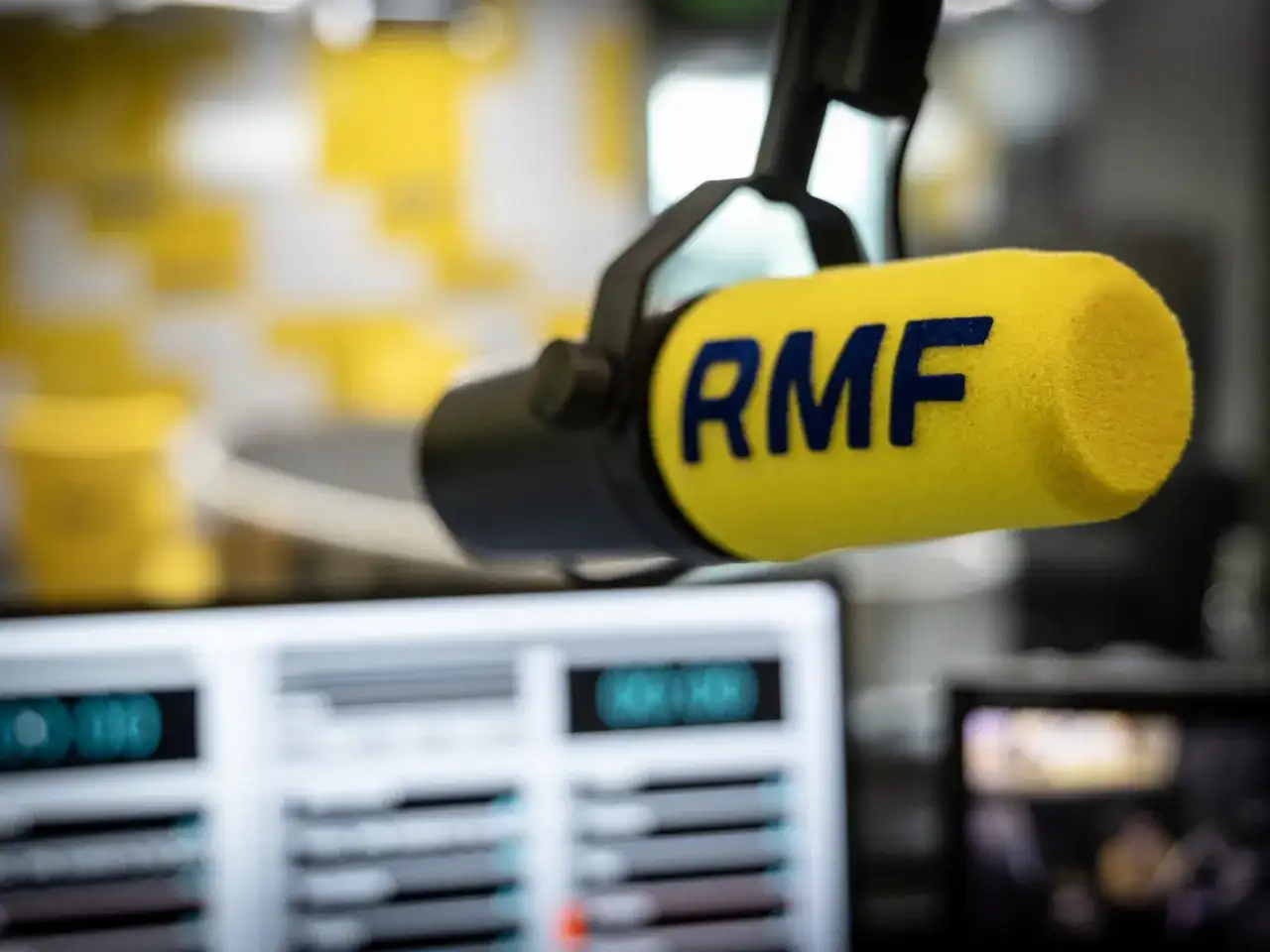 Mikrofon studyjny RMF FM na tle ekranów komputerowych.