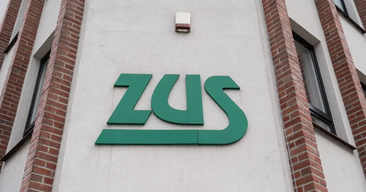 Zielone logo ZUS na jasnej ścianie budynku z ceglanymi elementami.