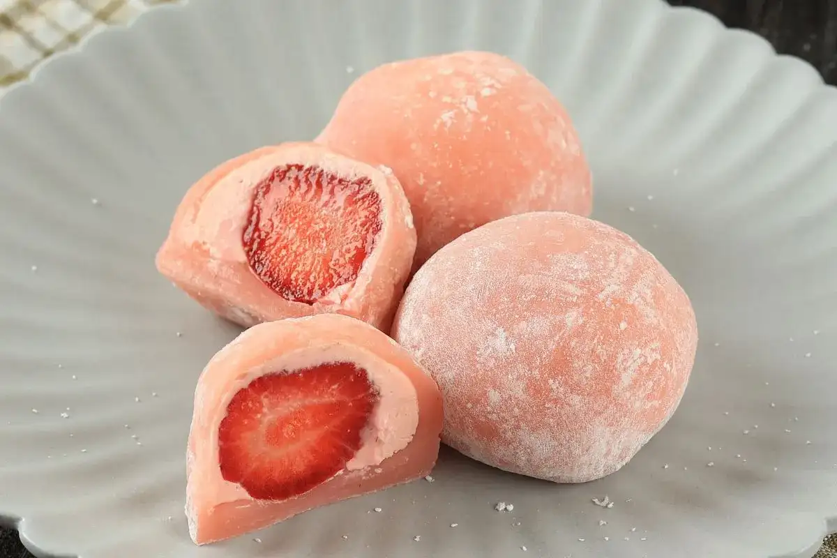 Różowe mochi z truskawkami na szarym talerzu.