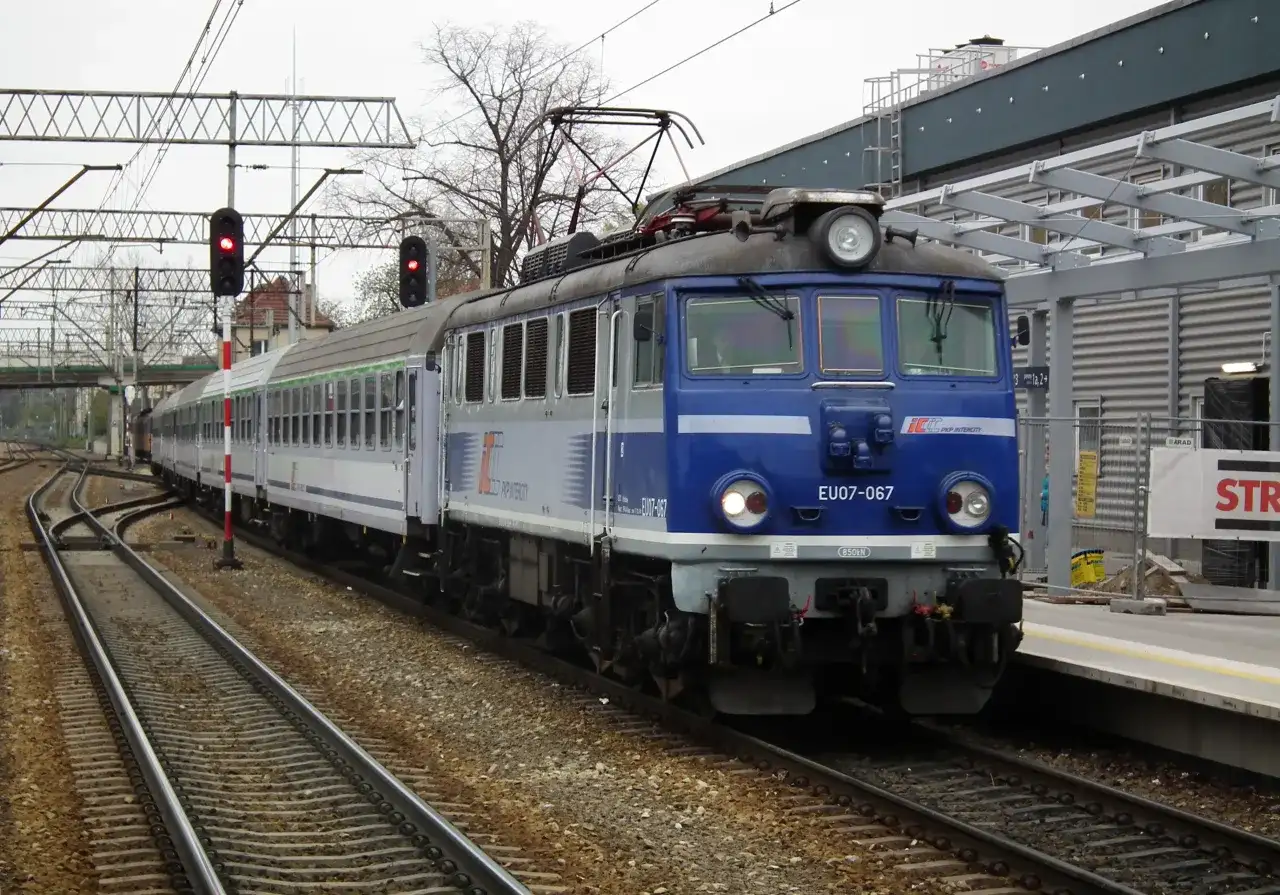 Niebieska lokomotywa PKP Intercity EU07-067 z wagonami na torach kolejowych.