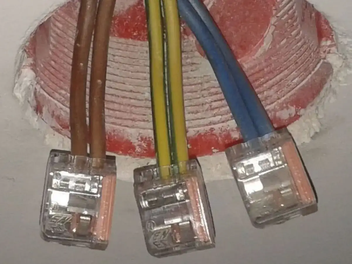 Żółto-zielony kabel oznacza uziemienie, kluczowy dla bezpieczeństwa instalacji elektrycznej. Widać go obok brązowych i niebieskich przewodów w puszkach.