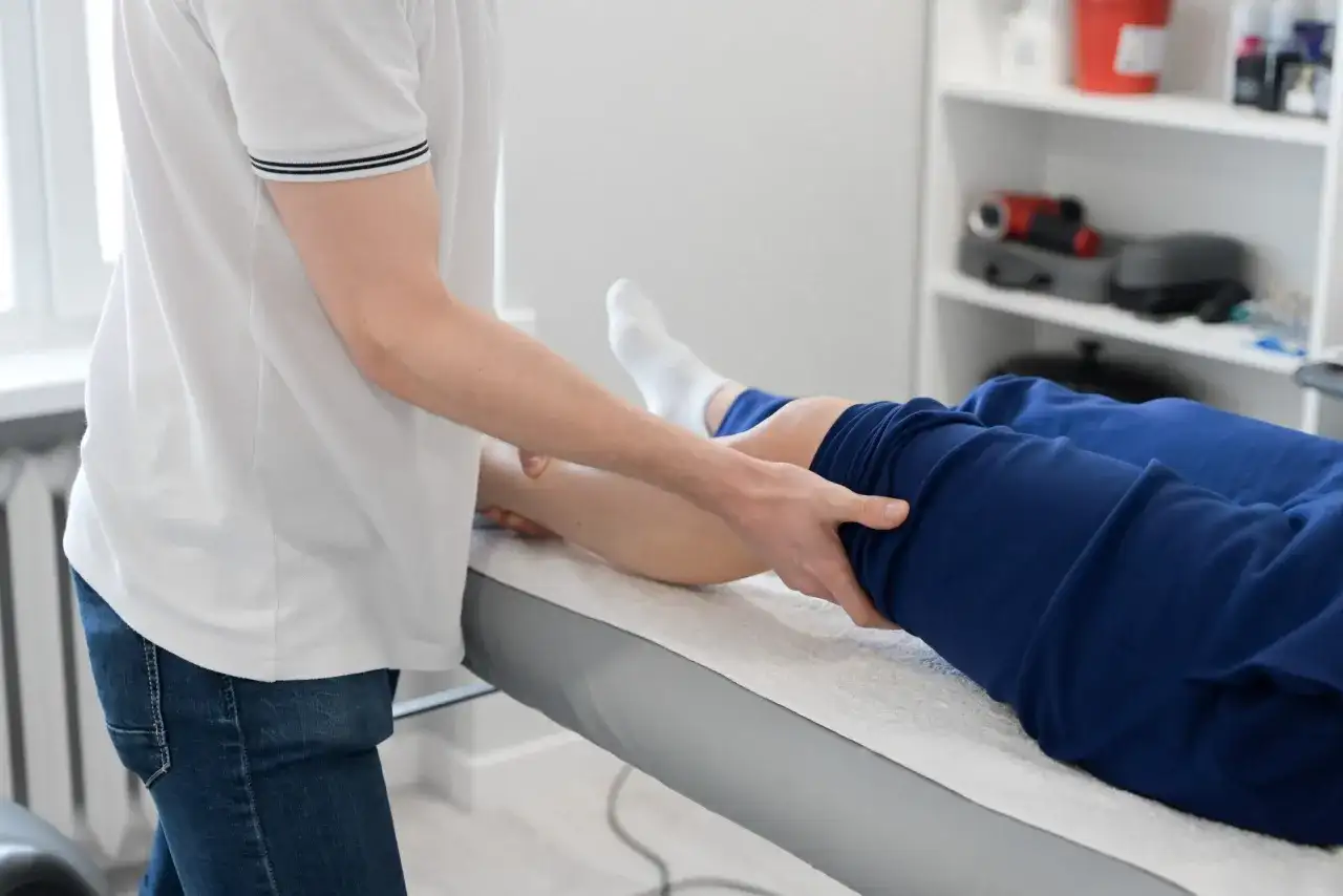 Fizjoterapeuta wykonuje masaż nogi pacjenta leżącego na kozetce.