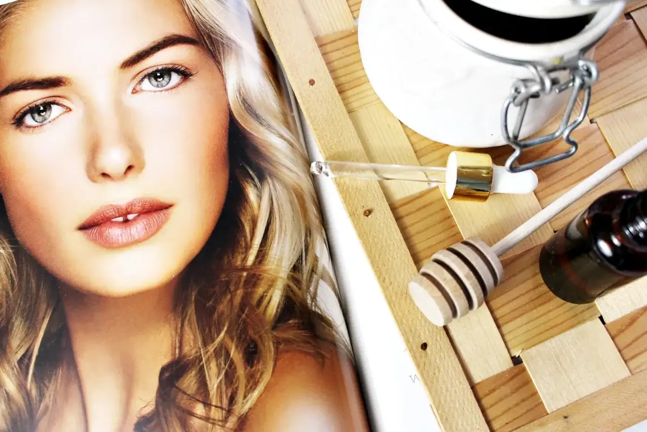 Odkryj, czym posmarować pryszcza! Na zdjęciu twarz modelki i akcesoria do pielęgnacji: pipetka z serum, miodek i buteleczka.