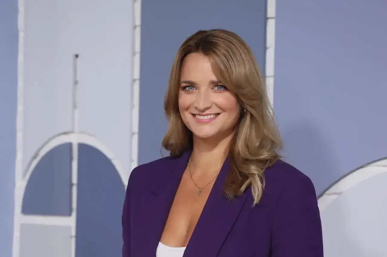 Dagmara Kaczmarek Szałkow w fioletowej marynarce, znana z Faktów TVN, uśmiecha się do kamery.
