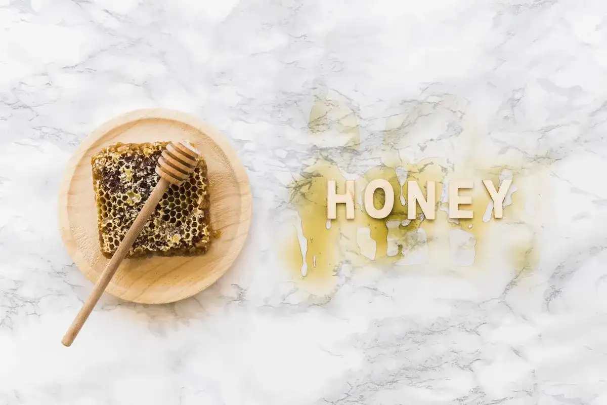 Plaster miodu z drewnianym mieszadełkiem na talerzyku i napis "HONEY" z miodu na marmurowym tle.