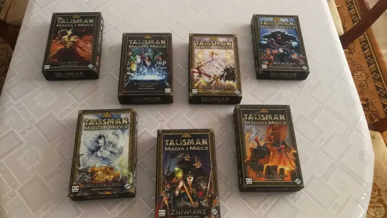 Pudełka z rozszerzeniami gry Talisman Magia i Miecz ułożone na obrusie.