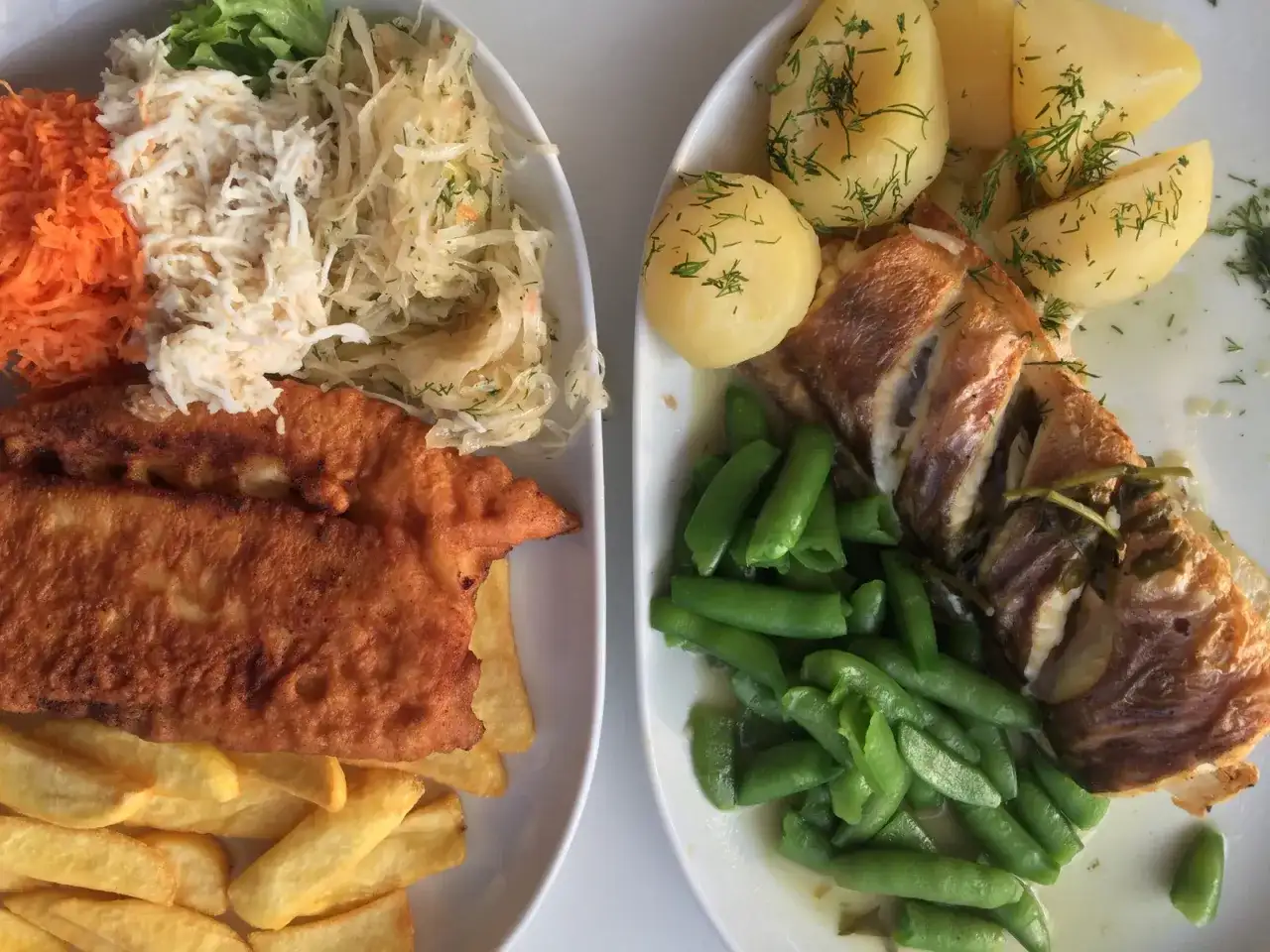 Dwa talerze pysznego jedzenia, idealne pytanie: gdzie zjeść w Gdyni? Ryba z ziemniakami i fasolką, a obok panierowany filet z frytkami i surówkami.