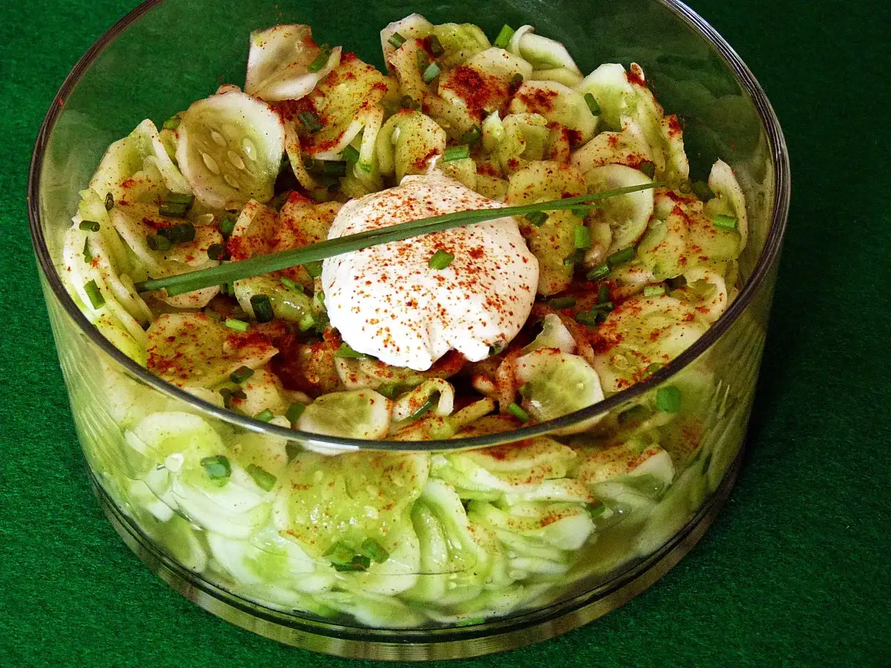 Sałatka z ogórków z koperkiem i papryką, udekorowana kleksem śmietany.