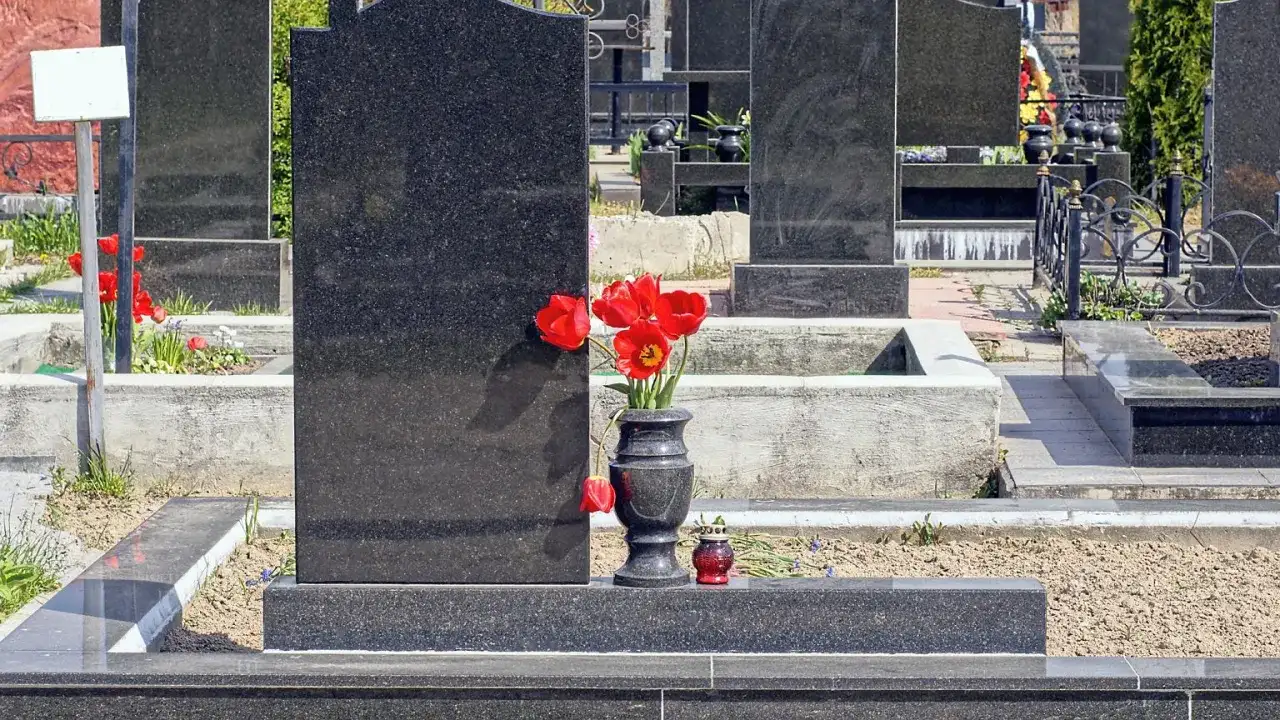 Cmentarz z nagrobkami z czarnego granitu, wazon z czerwonymi tulipanami i znicz.