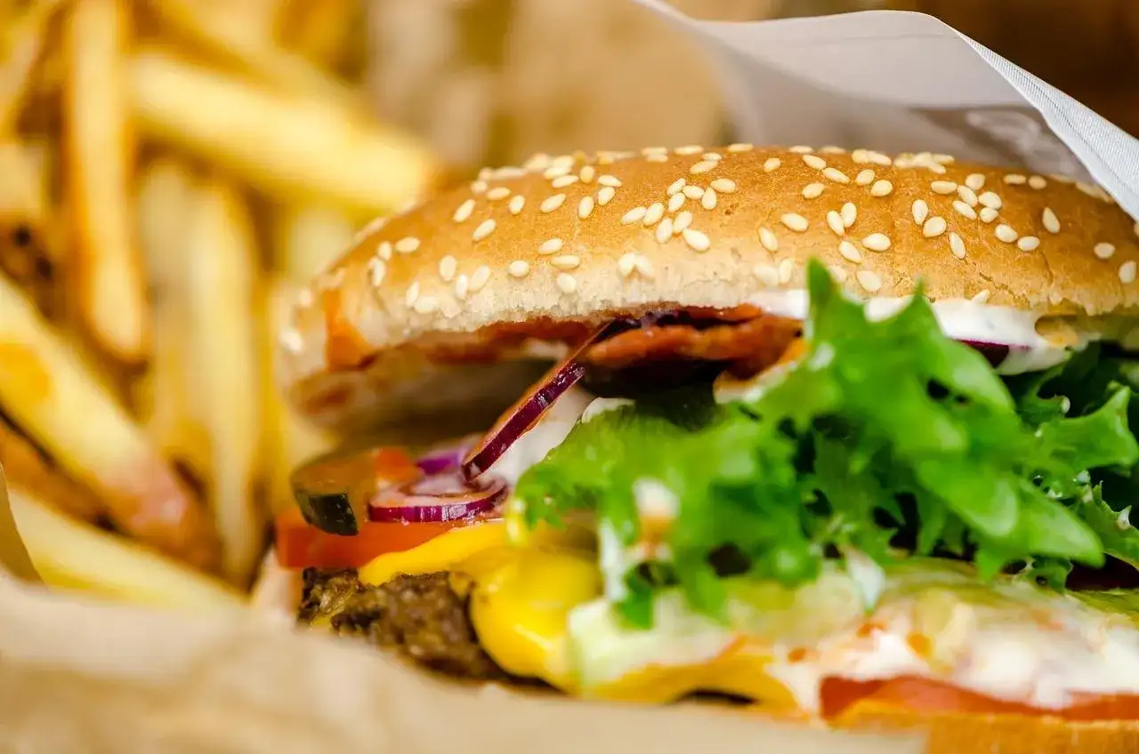 Soczysty burger wołowy z serem, warzywami i frytkami w papierowym opakowaniu.