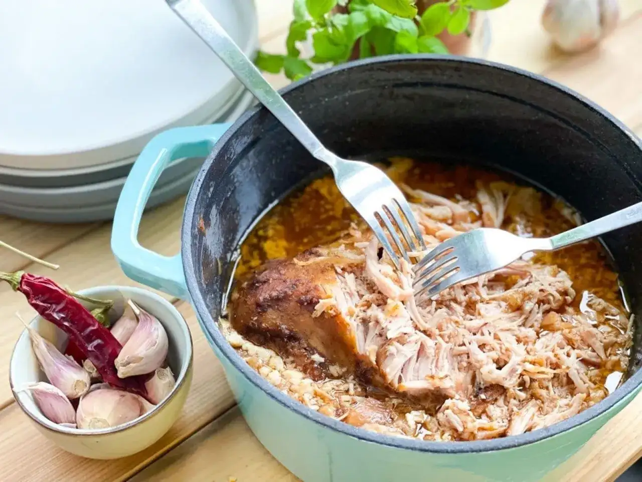 Szarpana wieprzowina w sosie, rozrywana widelcami w naczyniu żeliwnym, obok czosnek i papryczka chili.