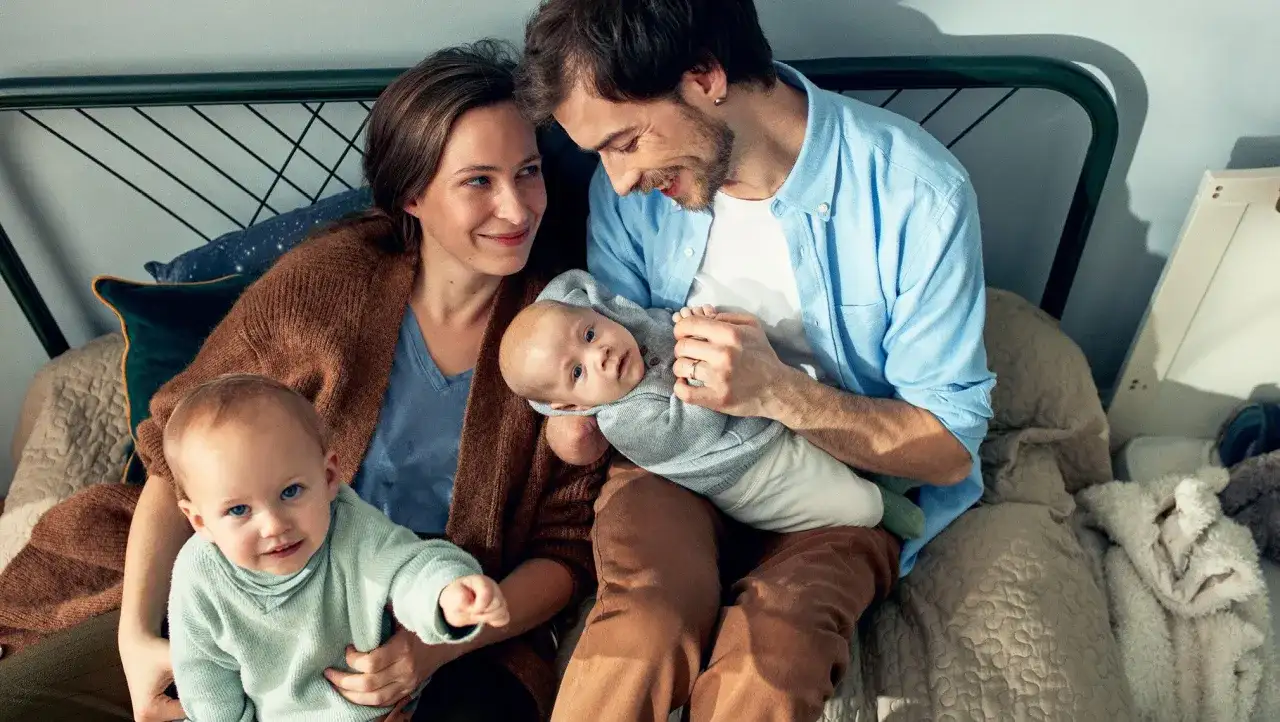 Rodzina z dwójką małych dzieci siedzi na łóżku.