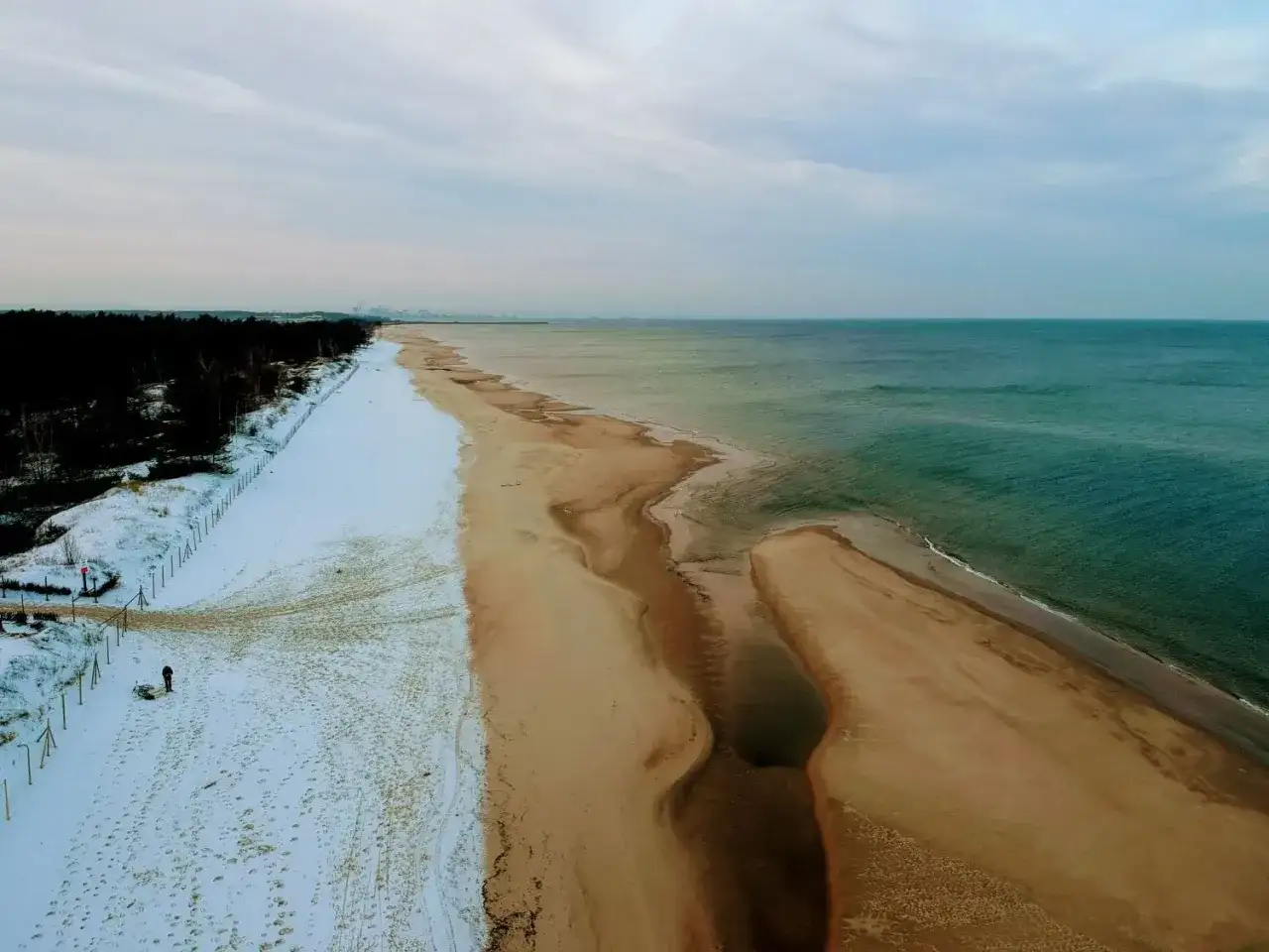 Plaża nad Bałtykiem zimą: śnieg, piasek i turkusowa woda.