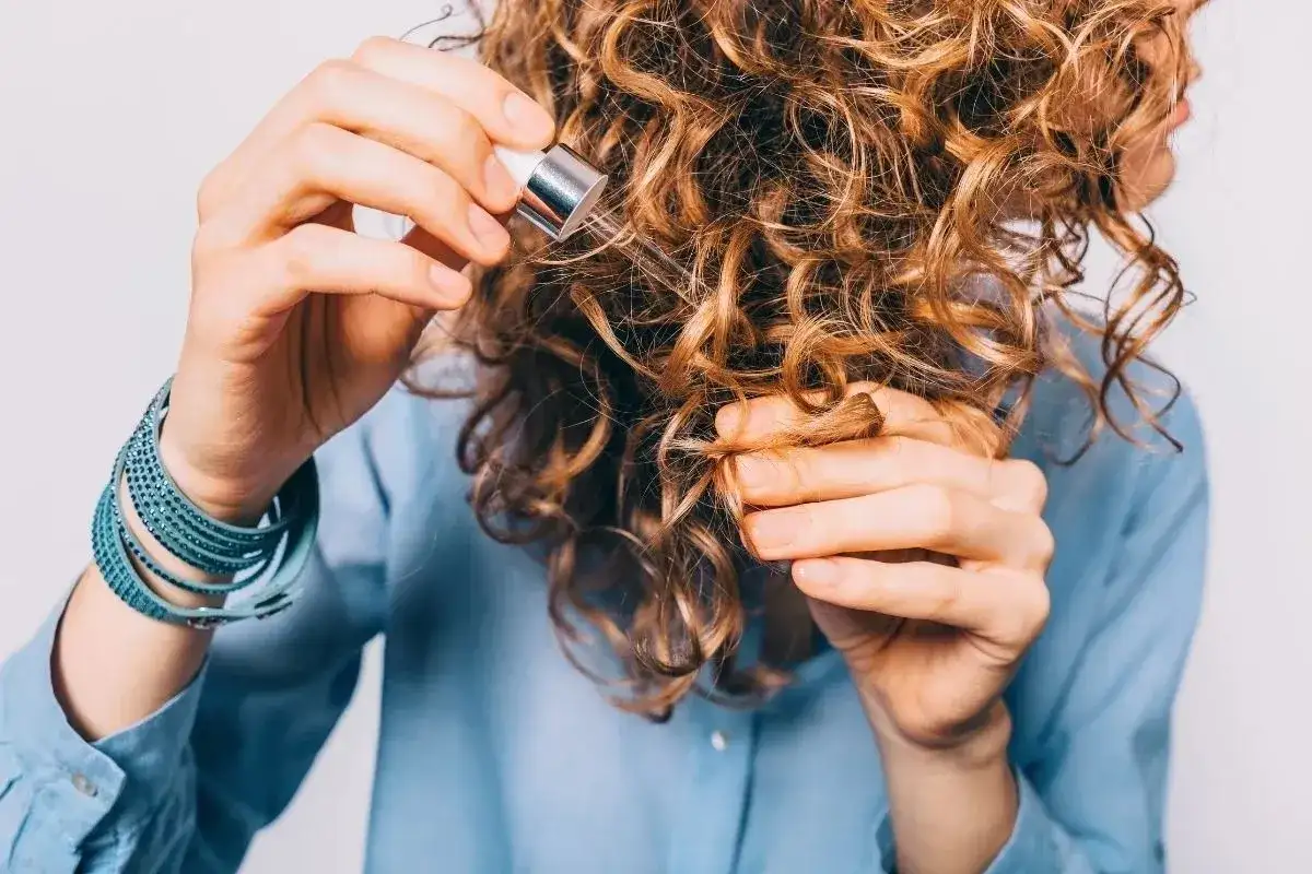 Kobieta z kręconymi włosami aplikuje serum. Czy serum do włosów się spłukuje? To pytanie nurtuje wiele osób dbających o fryzurę.