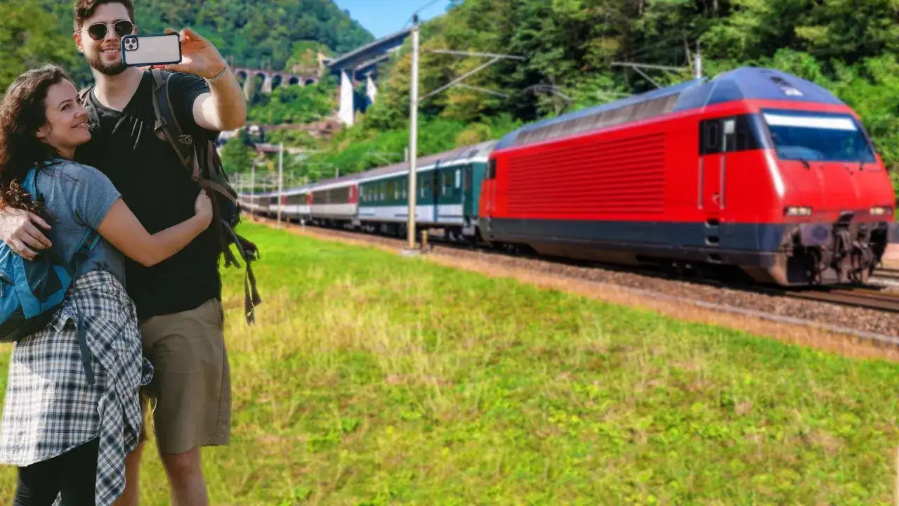 Para podróżnych z plecakami, którzy robią sobie selfie, na tle czerwonego pociągu jadącego w kierunku Krakowa Głównego i Bochni.