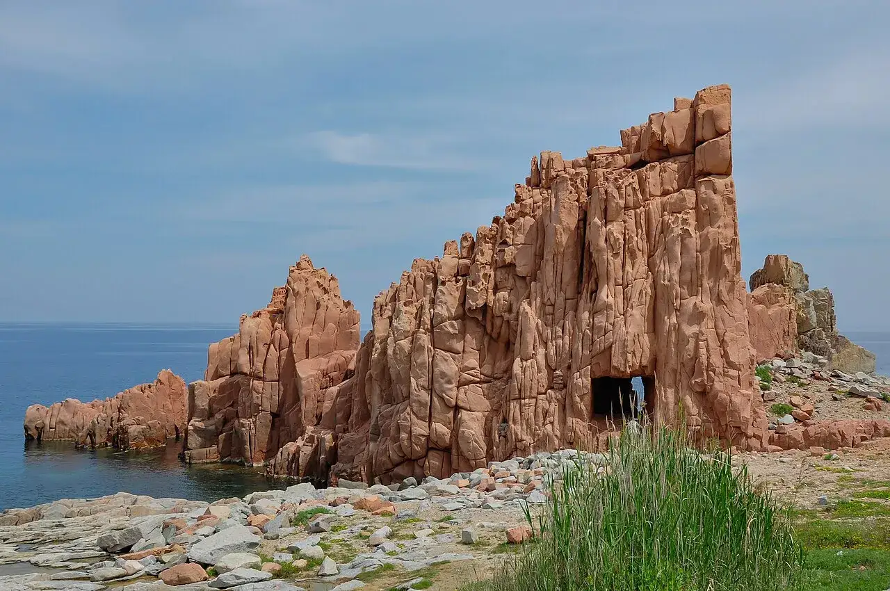 Scogliere rosse a picco sul mare blu, con un'apertura nella roccia. Un paesaggio suggestivo che ricorda il centro storico di Arbatax.