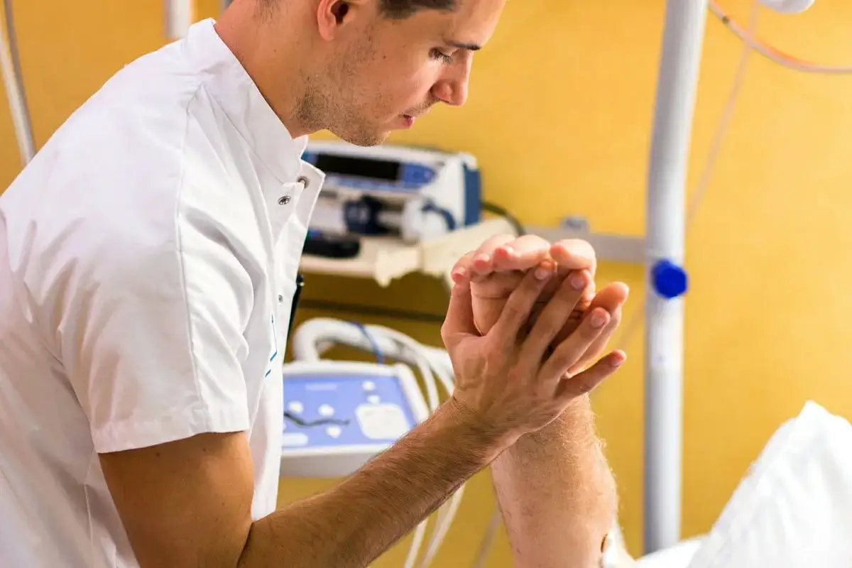 Fizjoterapeuta delikatnie masuje dłoń pacjenta, który jest 3 dni po udarze. Rehabilitacja jest kluczowa.