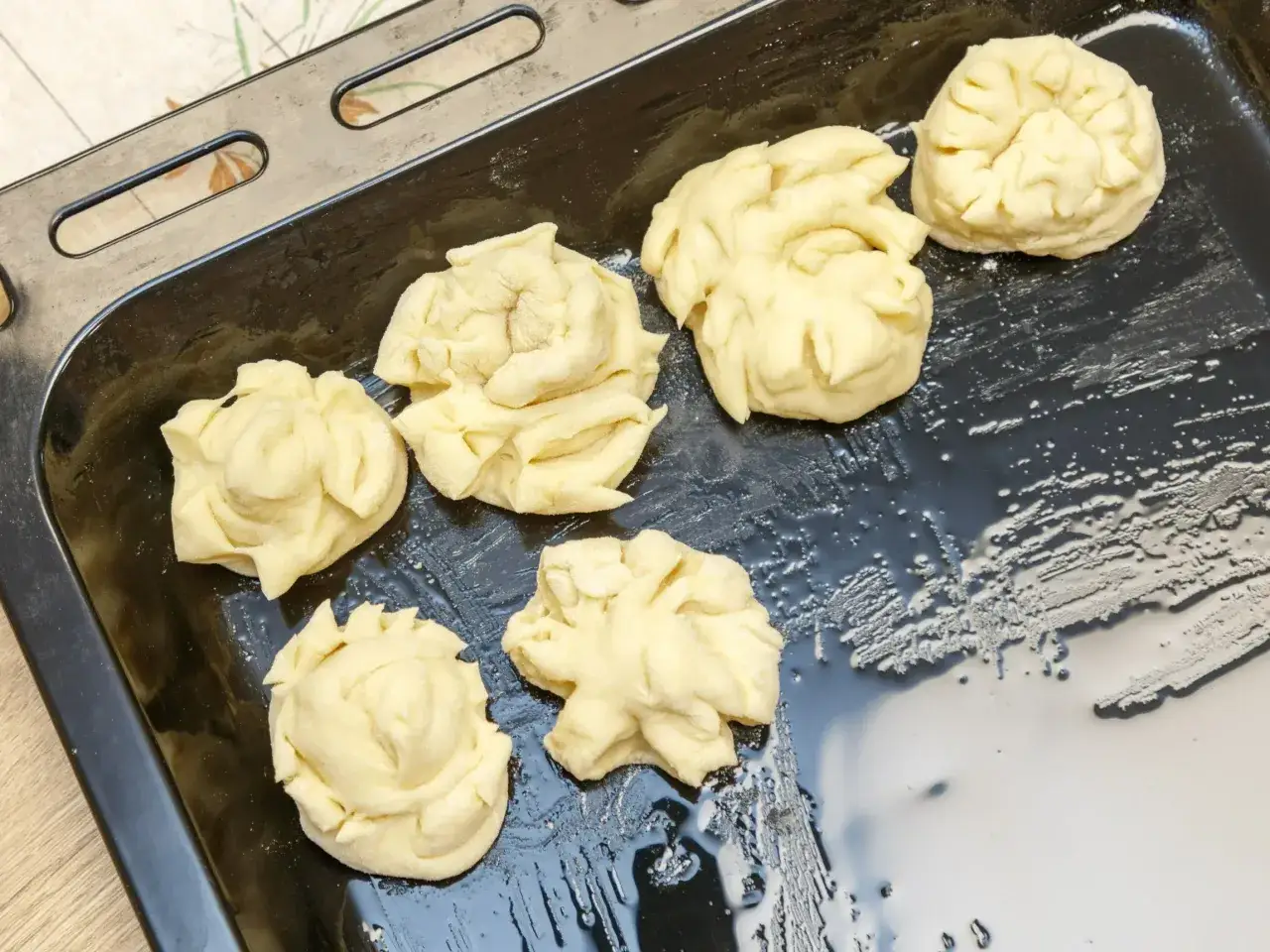 Surowe pączki z piekarnika ułożone na blasze. Ciasto ma kształt kwiatów, gotowe do pieczenia.