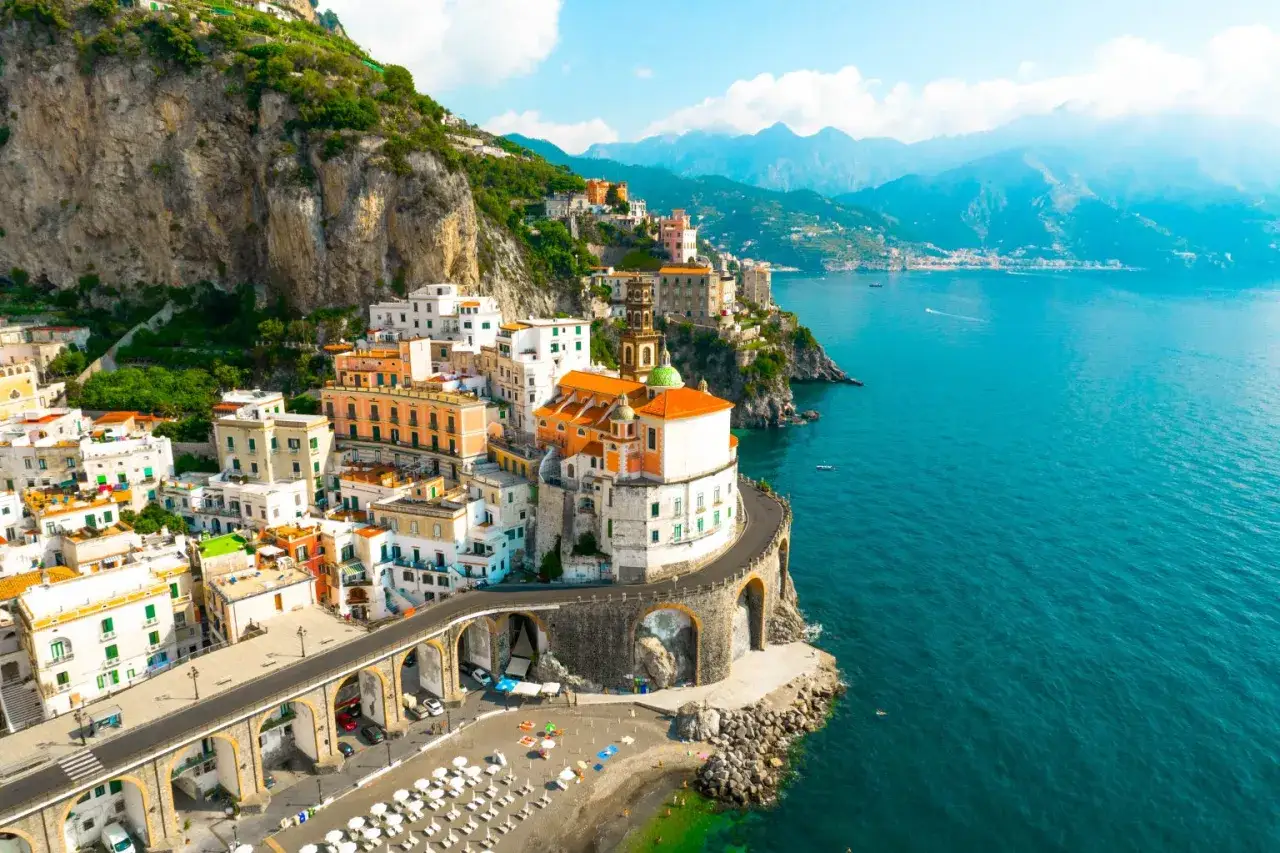 A picturesque coastal town with colorful buildings clinging to a cliffside, overlooking the turquoise sea. This view evokes the charm of the best beach towns in Sicily.