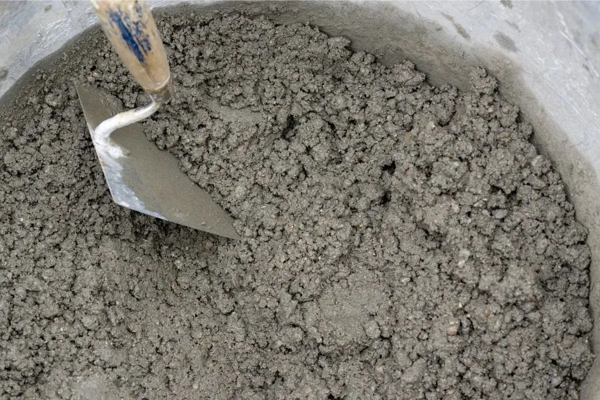 Secchio pieno di malta per intonaco esterno, con una cazzuola che affonda nel composto grigio.