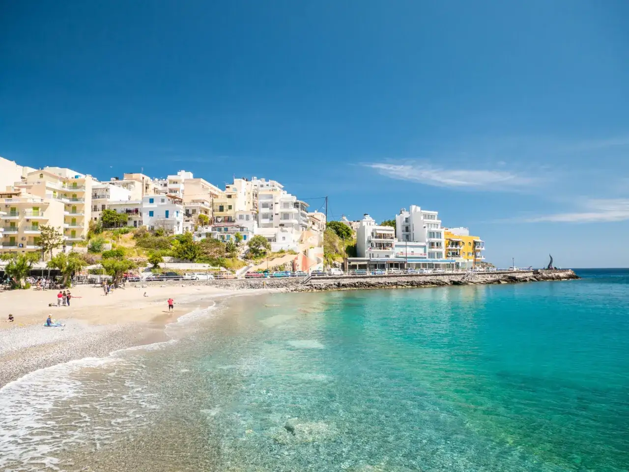 Malownicza plaża z białymi budynkami i turkusową wodą w Agios Nikolaos na Krecie.