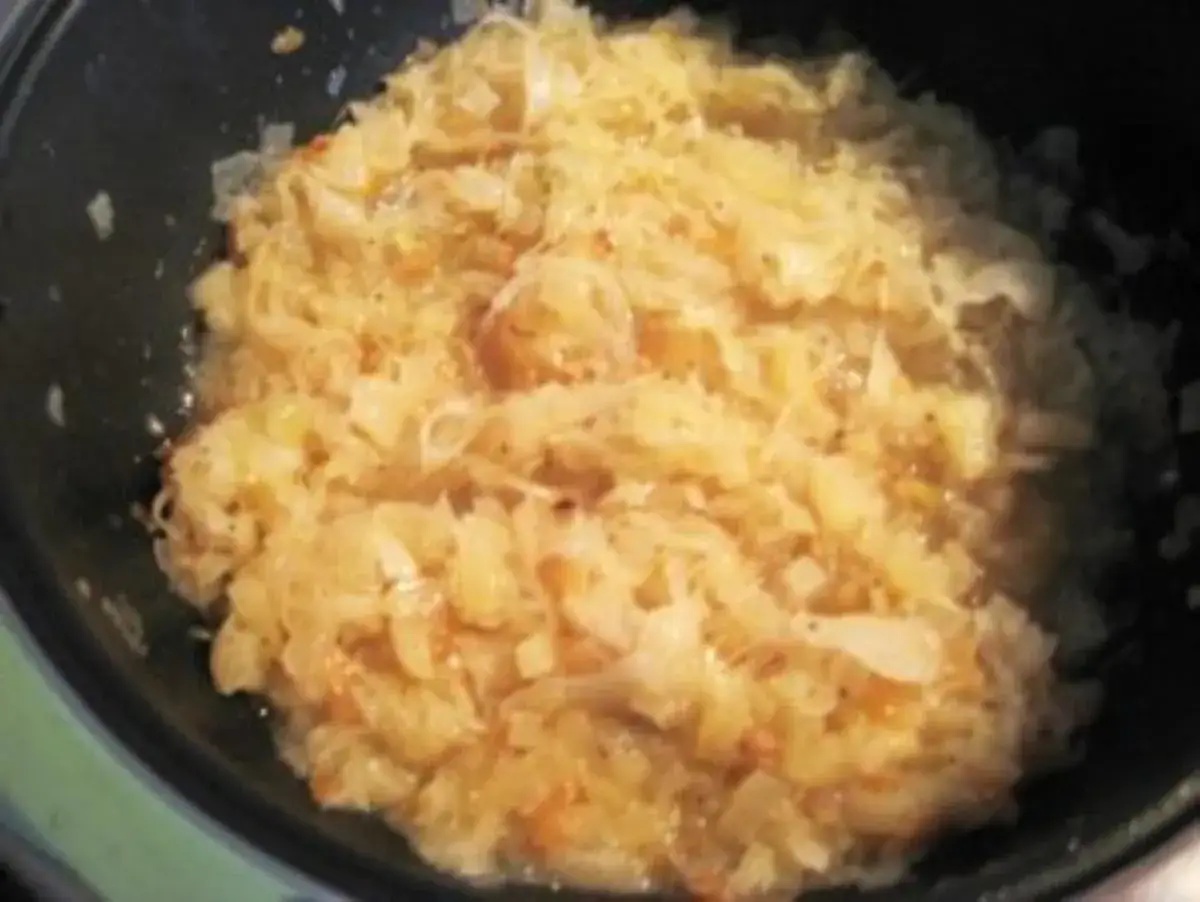 Sauerkraut kochen nach Omas Rezept: Ein Topf voller herzhaftem, gedünstetem Sauerkraut mit Zwiebeln und Gewürzen.