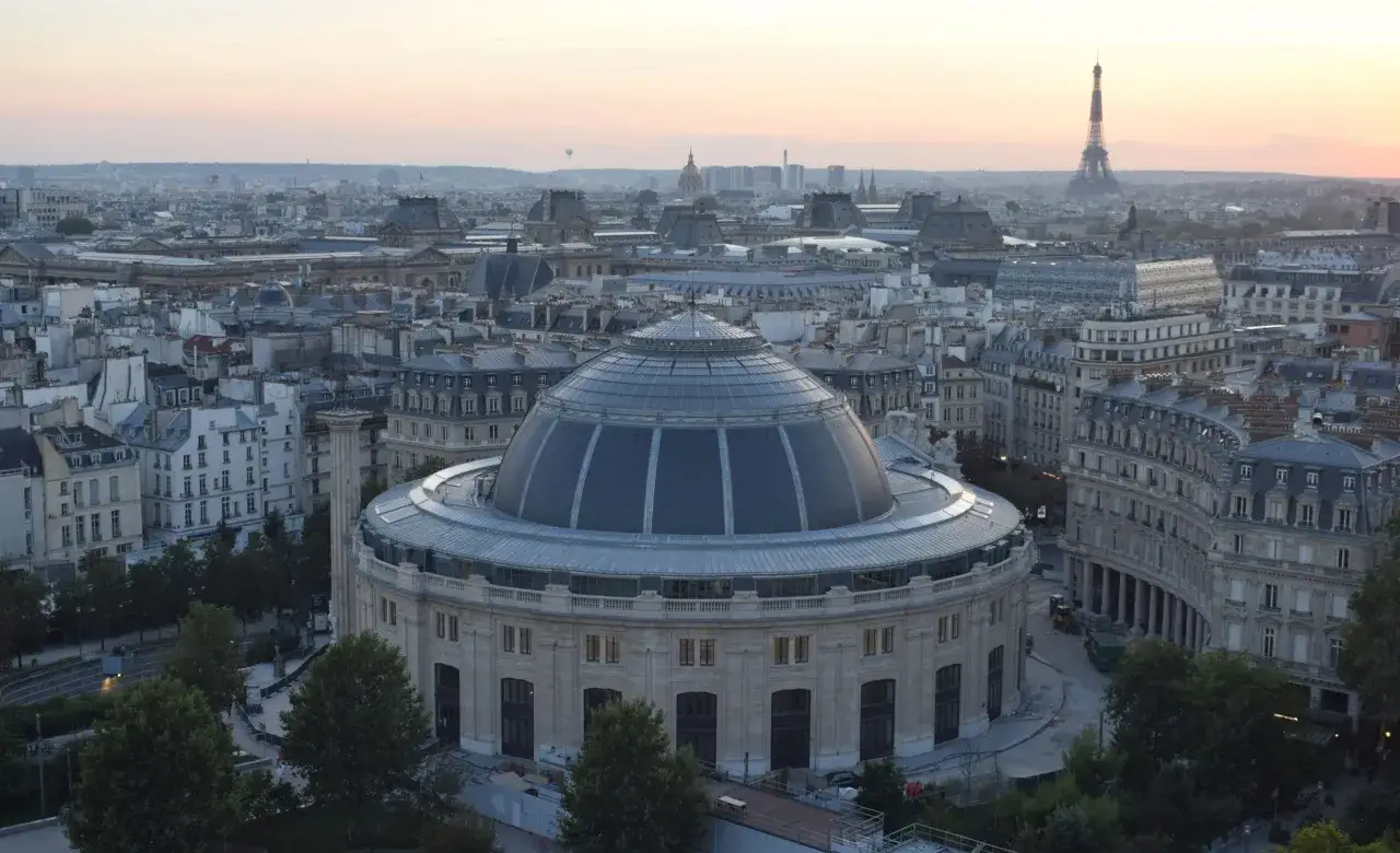 Vue a&eacute;rienne de Paris au cr&eacute;puscule, avec la coupole de la Bourse du Commerce au premier plan et la Tour Eiffel &agrave; l'horizon.