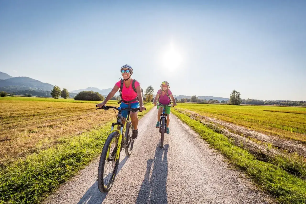 Zwei Frauen genießen Radtouren durch Deutschland. Sie fahren auf einem Feldweg, umgeben von grünen Feldern und Bergen.
