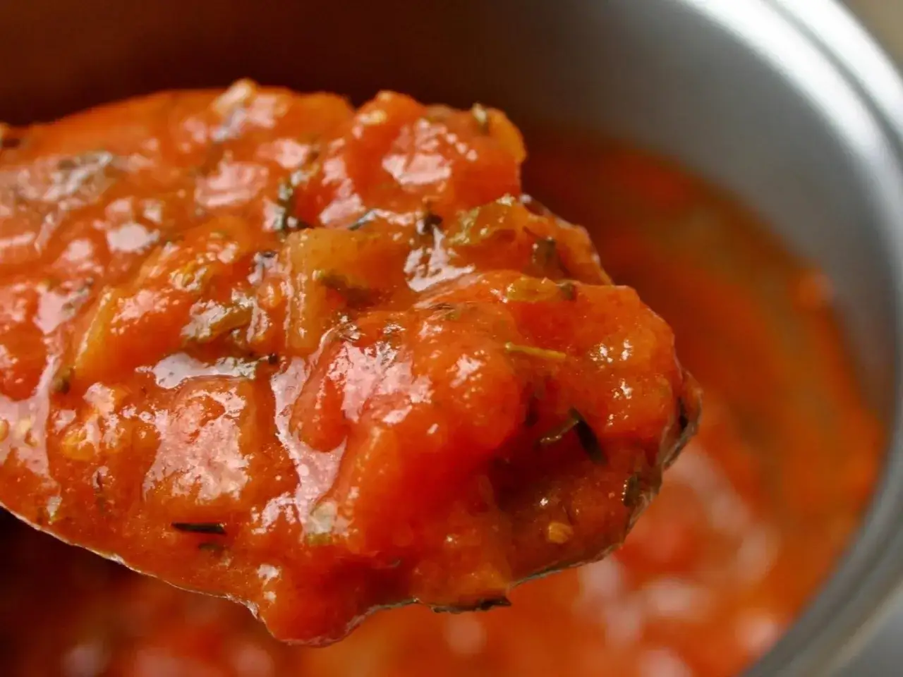Cuchara llena de sabrosa salsa de tomate casera, con trozos de tomate y hierbas aromáticas.