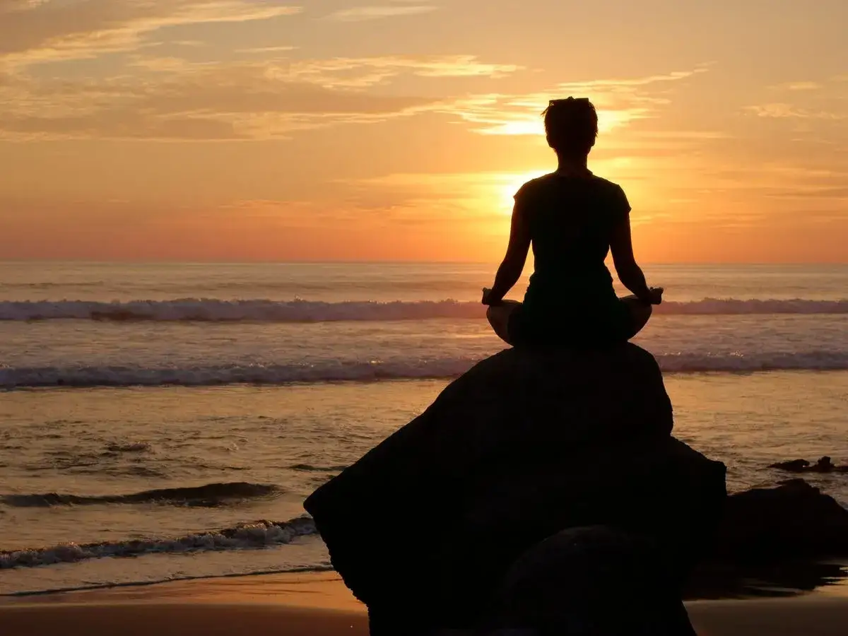 Silueta de persona meditando en una roca al atardecer, conectando con el yo superior.