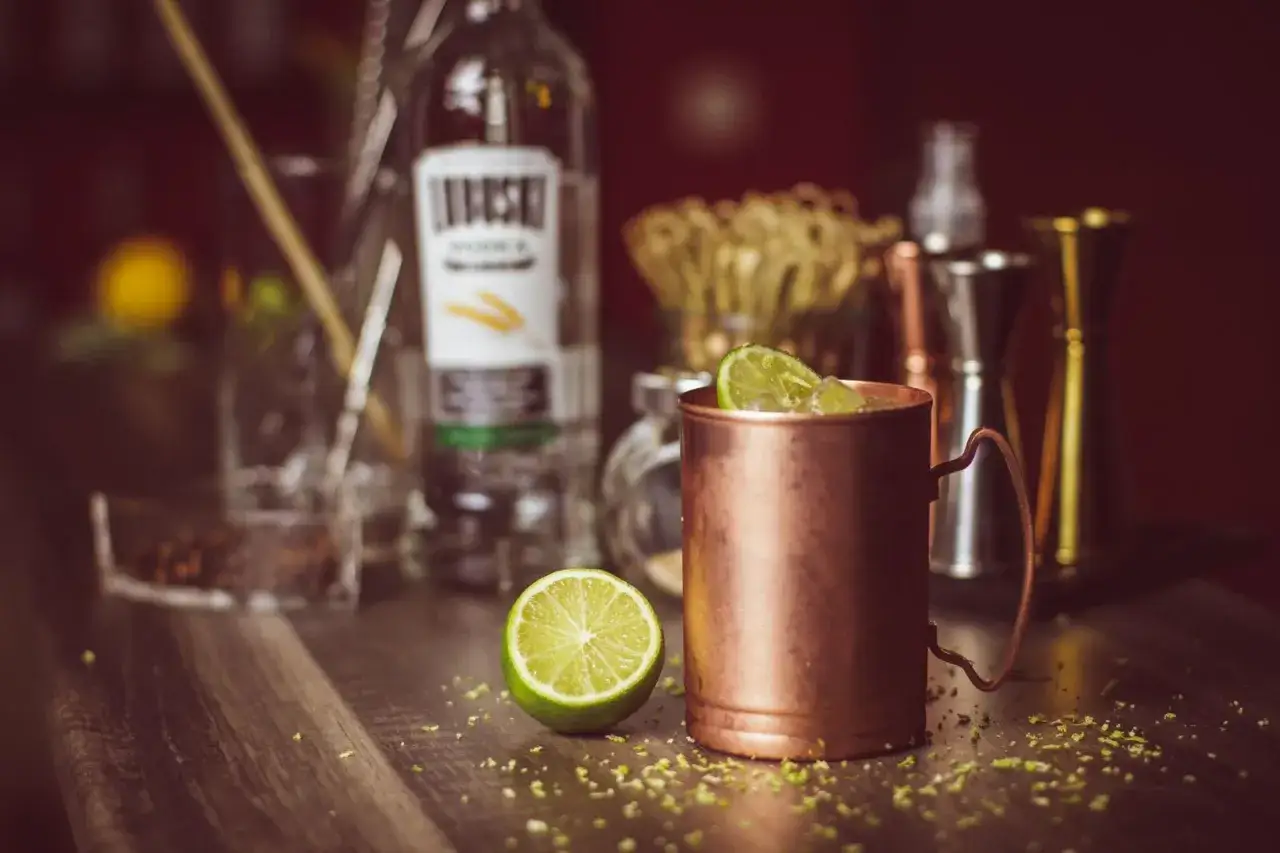 Miedziany kubek z Moscow Mule, limonka i butelka wódki. Różnica między piwem imbirowym a tonikiem imbirowym w drinku jest subtelna.