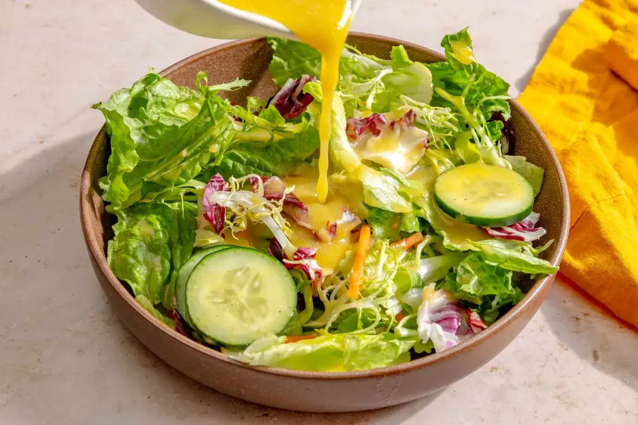A vibrant salad with lettuce, radicchio, cucumber, and carrots is being drizzled with a creamy miso dressing.