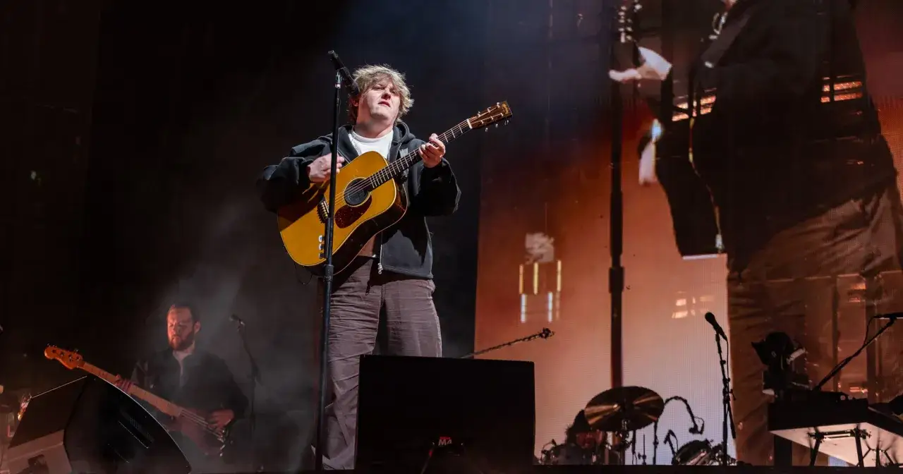 Lewis Capaldi gra na gitarze, mimo swojej choroby. Na scenie towarzyszy mu zespół.