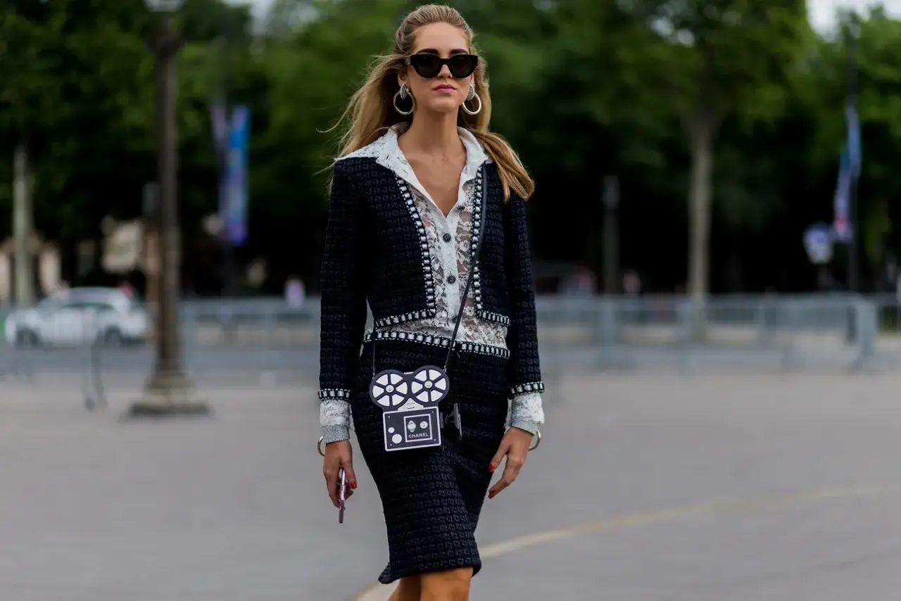 Elegancka kobieta w czarnej garsonce Chanel, białej koronkowej bluzce i okularach przeciwsłonecznych.