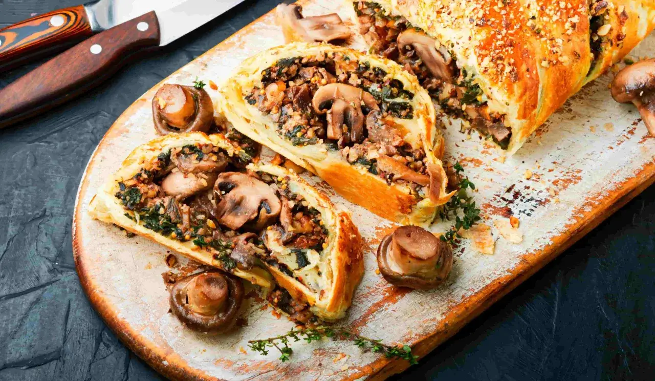 D&eacute;licieuse tourte aux champignons, garnie de l&eacute;gumes verts et de noix, coup&eacute;e en tranches sur une planche en bois.
