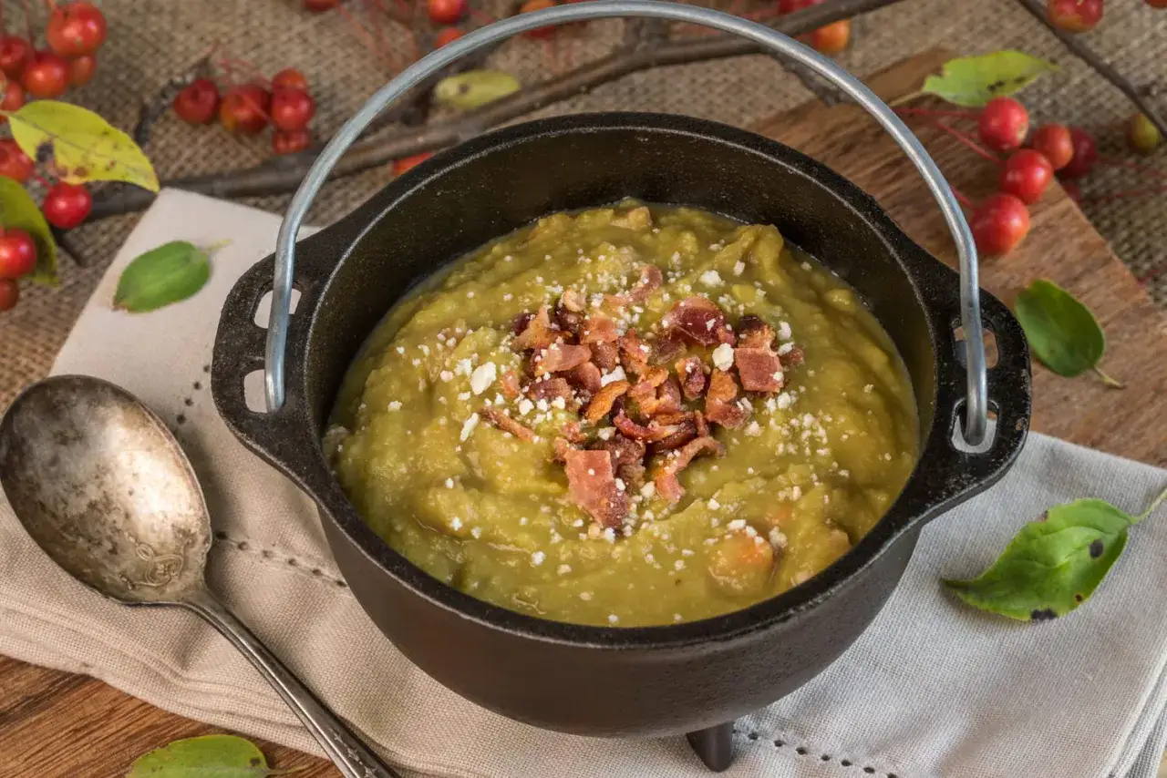 Un chaudron de pois cassés crémeux, garni de lardons croustillants et de fromage râpé, prêt à être dégusté.