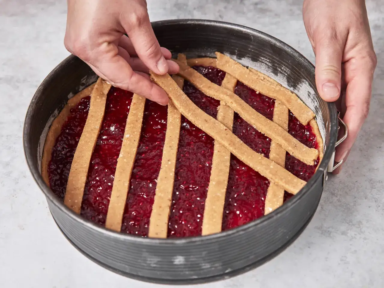 H&auml;nde legen Gitterstreifen auf eine fruchtige F&uuml;llung f&uuml;r eine Linzer Torte in einer Springform.