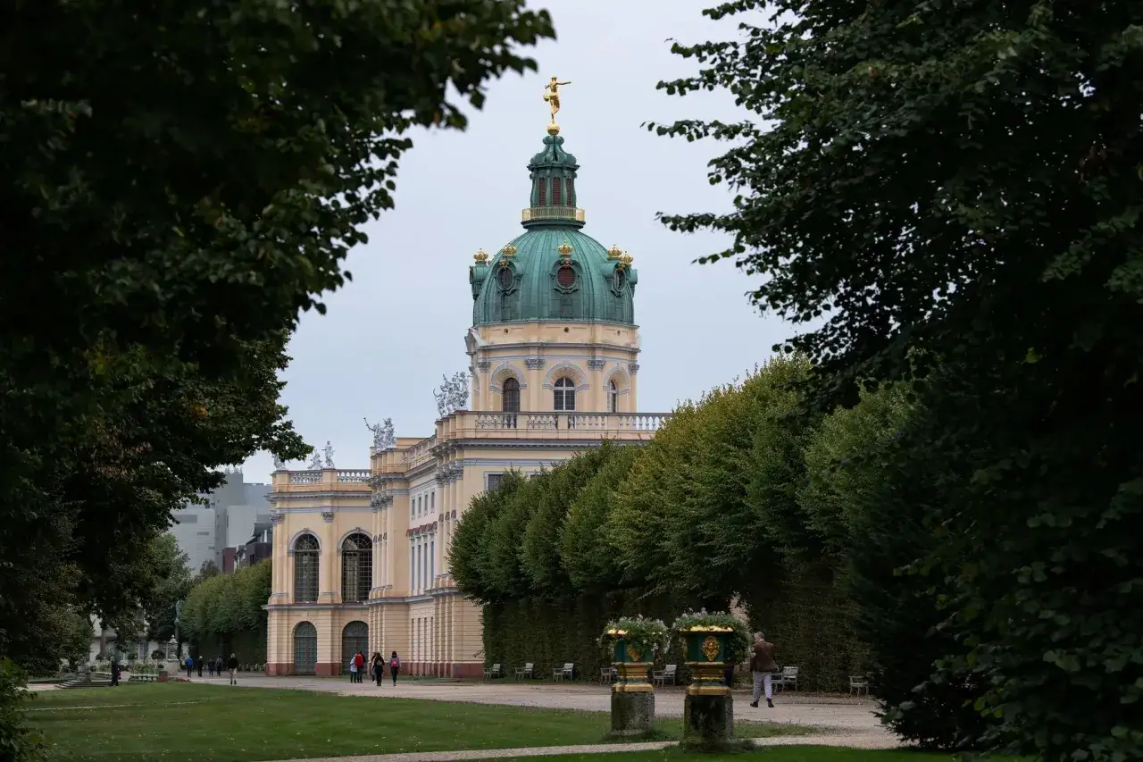 Ein prachtvolles Schloss in Berlin, mit einer gr&uuml;nen Kuppel und einer goldenen Statue, umgeben von B&auml;umen und einem gepflegten Garten.